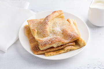 A plate of traditional finnish or danish pancakes pannukakku sprinkled with powdered sugar with sour cream and jam on a light background. Delicious vegetarian homemade breakfast