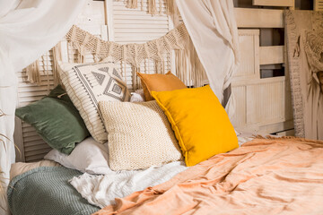 Modern home interior design. Bed with canopy and orange colored pillows, blanket. bedroom interior, scandinavian style.Cozy room in apartment with design in style of the boho chic. Comfortable bed