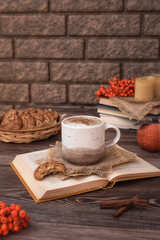 Cozy autumn still life: a cup of coffee, a basket of cookies, a book, cinnamon sticks, candles and bunches of rowan on a dark wooden table. Rustic still life. 