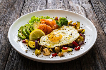 Keto diet - smoked salmon, sunny side up egg, avocado and mix of vegetables on wooden table
