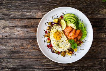 Keto diet - smoked salmon, sunny side up egg, avocado and mix of vegetables on wooden table
