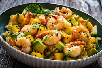 Fusilli with prawns, mango, avocado and mint on wooden table
