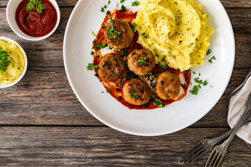 Fried pork meatballs with potato puree and tomato sauce on wooden table
