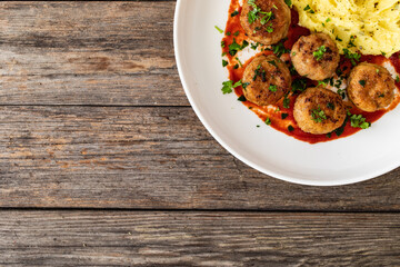 Fried pork meatballs with potato puree and tomato sauce on wooden table
