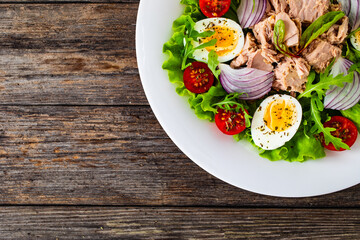 Tuna salad - tuna, hard boiled eggs, cherry tomatoes, lettuce and onion on wooden table
