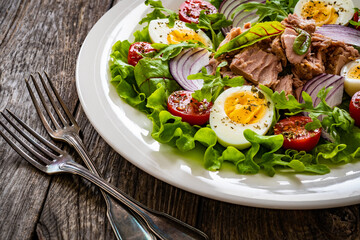 Tuna salad - tuna, hard boiled eggs, cherry tomatoes, lettuce and onion on wooden table
