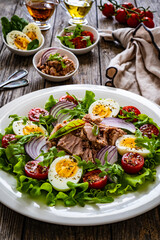 Tuna salad - tuna, hard boiled eggs, cherry tomatoes, lettuce and onion on wooden table
