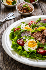 Tuna salad - tuna, hard boiled eggs, cherry tomatoes, lettuce and onion on wooden table
