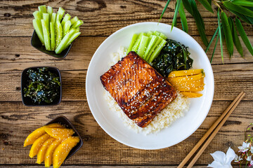 Fried teriyaki salmon steak with white rice, mango, cucumber and wakame on wooden table
