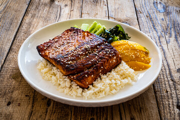 Fried teriyaki salmon steak with white rice, mango, cucumber and wakame on wooden table

