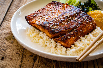Fried teriyaki salmon steak with white rice, mango, cucumber and wakame on wooden table
