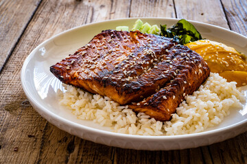 Fried teriyaki salmon steak with white rice, mango, cucumber and wakame on wooden table
