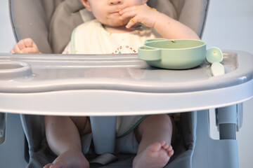 A small child sits on a high chair and eats vegatables. baby eating