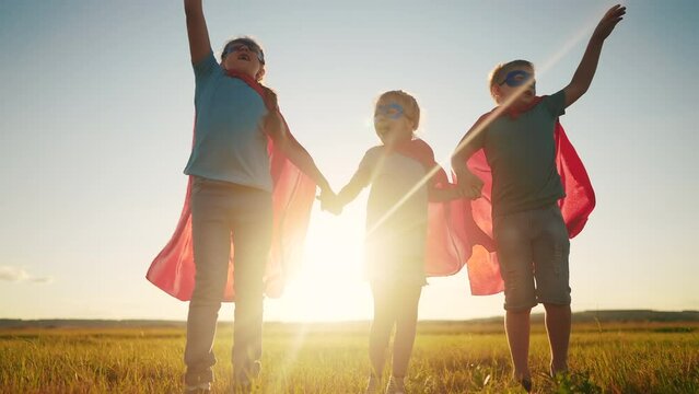 team superhero. a group of children are dream running across the field in a superhero costume with a silhouette of a red cape at sunset. the concept of a happy family childhood. teamwork superhero
