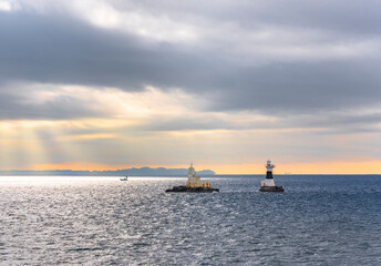 Fototapeta premium Lighthouse and oceanographic observation station of Ashikashima in the sea of the Uraga channel of Tokyo bay with a boat sailing along the Boso peninsula coasts in the morning light below a cloudy sky