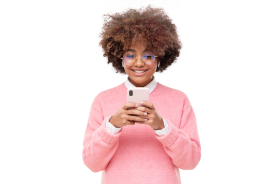 African american smiling teenage girl with afro hairstyle holding smartphone with both hands, chatting with friend, using social media app
