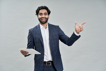 Happy young arab business man executive pointing while holding digital tablet presenting new online product or website, advertising trainings or free elearning webinars standing isolated on beige.