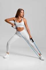 Fitness woman working out with resistance band on gray background. Athletic girl exercises with...