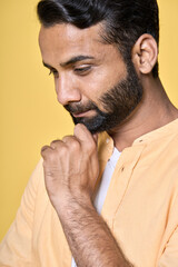 Fototapeta premium Smiling thoughtful calm mindful indian man thinking, dreaming, feeling mental balance, pensive, lost in thoughts, meditating, reflecting isolated on yellow background. Vertical close up portrait.