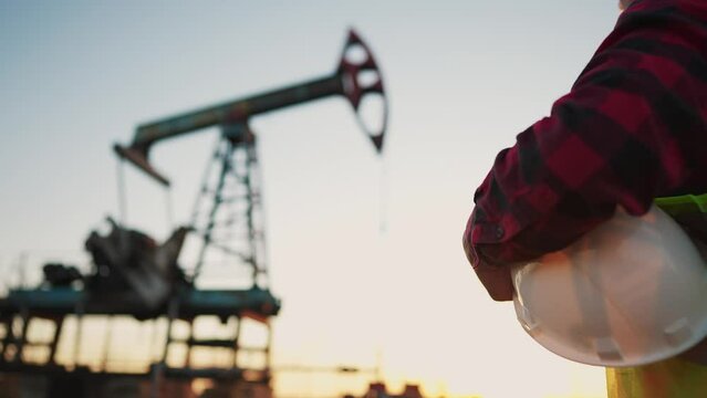 oil production. a worker holding a protective hard hat at sunset in the background an oil pump. oilfield business a extraction concept. oil extraction pump. lifestyle oil pump rig