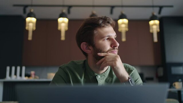 man works with laptop at home or in co-working space, frontal portrait of handsome bearded guy