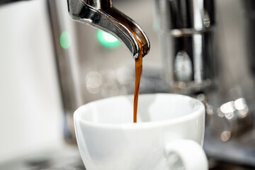 Coffee coming out of an Italian espresso coffee machine, flowing into a small, white espresso cup