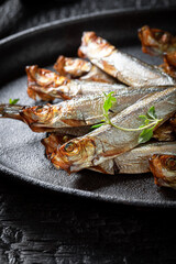 Salty smoked sprats on a black plate and burnt table.