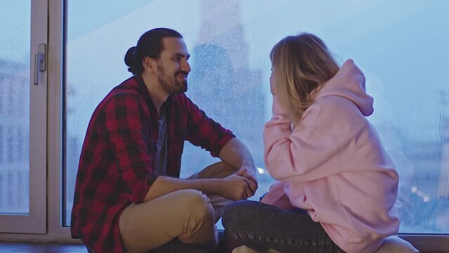 Portrait of two lovers sitting comfortably by the window on a rainy evening