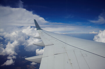 Fototapeta na wymiar Airplane wing over landscape with white clouds in blue sky