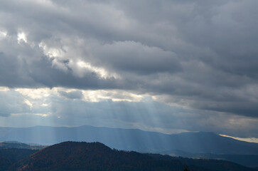 Scenic autumn mountain landscape with rays of light through cloudy sky. Carpathian Mountains, Ukraine