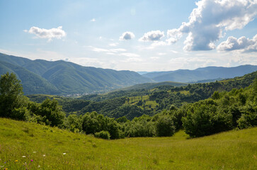 Countryside landscape with grassy pasture on the rolling hills and village in the valley near mountain ridge in sunny summer day. Carpathian Mountains, Ukraine