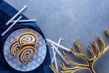 Hanukkah desert plate with nut roll , white candles, and golden menorah on textured blue background