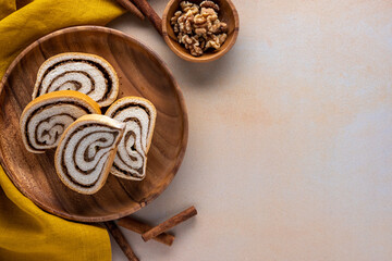 sliced nut roll on a wood plate with small bowl of walnuts cinnamon sticks and napkin on a textured background