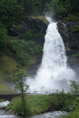 Wonderful landscapes in Norway. Vestland. Beautiful scenery of  Steinsdalsfossen waterfall from the Fosselva river. Mountains, trees in background. Rainy day. Selective focus