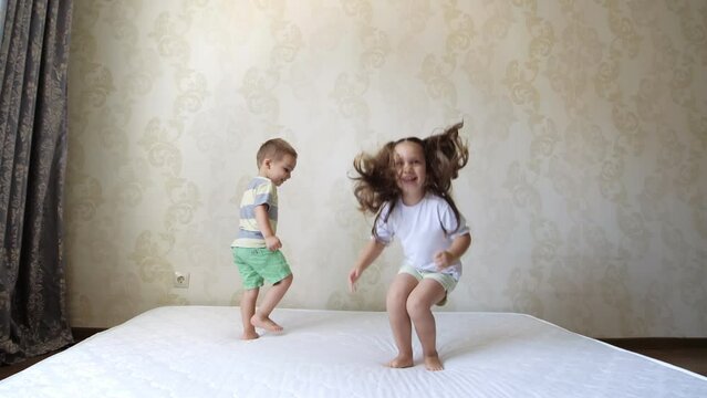 Happy funny little children, brother and sister, jumping on mattress. Cheerful cute active kids having fun playing during the repair.Leisure activity, lot of energy, hyperactive kid concept.Childhood.