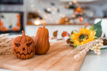 Autumn flowers, Jack's pumpkin and candles on a tray. In the background is the interior of a white Scandi-style kitchen. The concept of home and comfort. Autumn decor for Halloween.