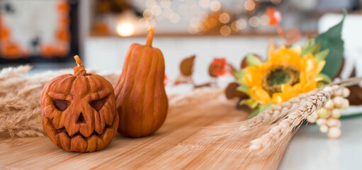 Autumn flowers, Jack's pumpkin and candles on a tray. In the background is the interior of a white Scandi-style kitchen. The concept of home and comfort. Autumn decor for Halloween.