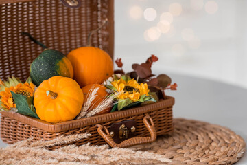 Fototapeta na wymiar Home warmth. Still-life. Pumpkins, a wicker basket, candles and flowers. In the background is the interior of a white Scandi-style kitchen. The concept of home and comfort. Autumn decor for Halloween.
