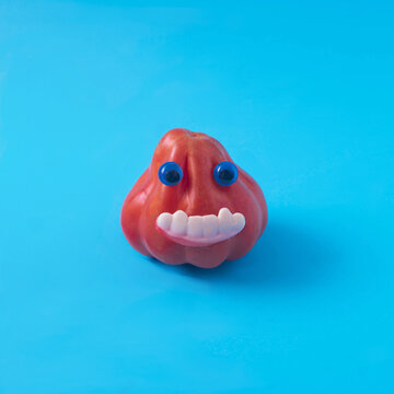 A tomato with blue eyes and theets on blue background. Minimal surreal creative concept for Halloween celebration banner or party invitation.