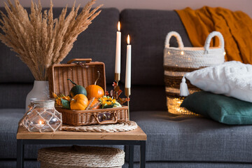 Cozy autumn concept. Home warmth in cold weather. Still-life. Pumpkins, wicker basket, candles and flowers on the coffee table in the home interior of the living room.