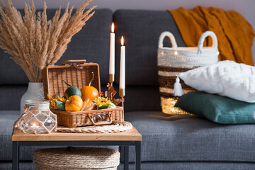 Cozy autumn concept. Home warmth in cold weather. Still-life. Pumpkins, wicker basket, candles and flowers on the coffee table in the home interior of the living room.