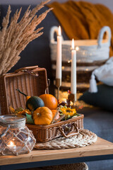 Cozy autumn concept. Home warmth in cold weather. Still-life. Pumpkins, wicker basket, candles and flowers on the coffee table in the home interior of the living room.