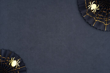 Black paper fans with golden cobwebs and golden glittering spiders on a dark background. The scary Halloween decoration on black with copy space. Halloween theme for your creativity.