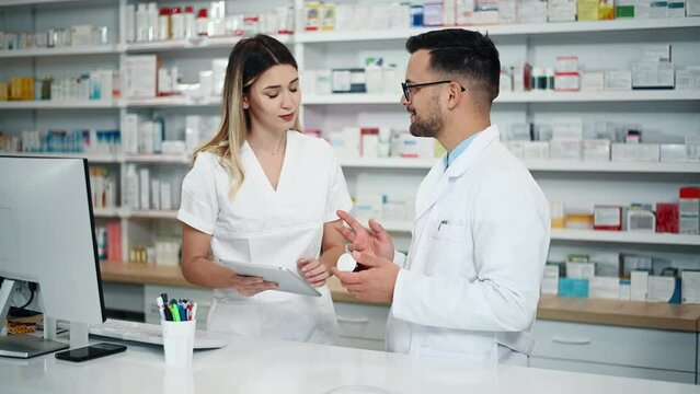 Happy young male and female colleagues pharmacist working in a pharmacy. Discussing about new medicine.