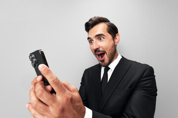 Man businessman in suit holding phone in hand on phone posing in front of smartphone camera with smile with teeth happy surprise win on gray background close-up face wide camera angle, technology