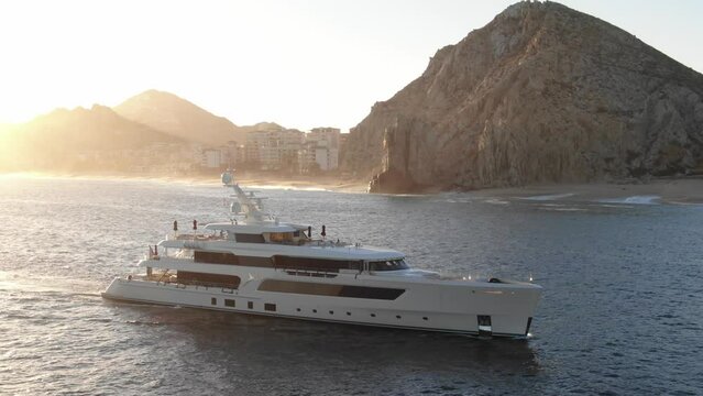 Aerial of Mega Yacht in bay of Cabo San Lucas at sunset with mountains in background