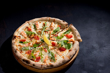 Pizza with salmon, mozzarella, cherry tomatoes, arugula, lemon and parmesan. Italian cuisine. On a black background. Free space for text. View from above.