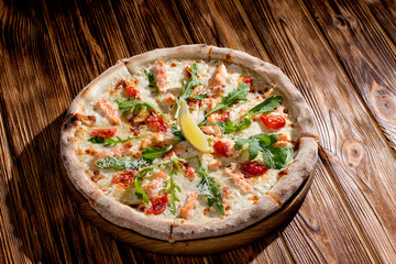 Pizza with salmon, mozzarella, cherry tomatoes, arugula, lemon and parmesan. Italian cuisine on a woden background