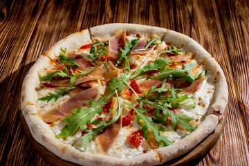 Pizza with jamon and prosciutto, mozzarella, cherry tomatoes, arugula and parmesan on a wood background. Italian cuisine.