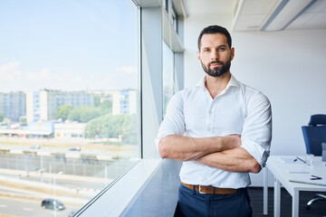 Businessman standing at office looking at camera. Portrait of male entrepreneur